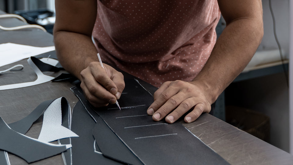 À l'atelier de Pia (66) : les mains de l'artisan tracent des repères blancs sur une pièce noire, entourée de pièces déjà découpées.
