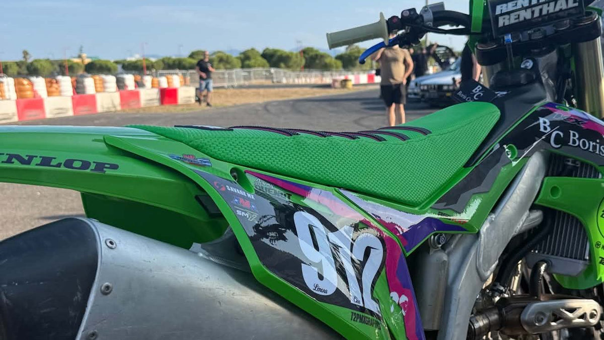 Housse de selle BKS verte en matière grip, ribs noirs à liseré rose, sur une Kawasaki KX 250 F au paddock