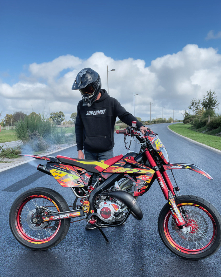 Pilote casqué debout à côté d'une moto rouge et jaune préparée, sur route