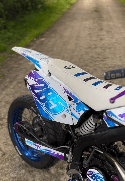 Gros plan sur l'arrière d'un 50 en roues route bleu, violet et blanc, numéro 285, housse de selle blanche