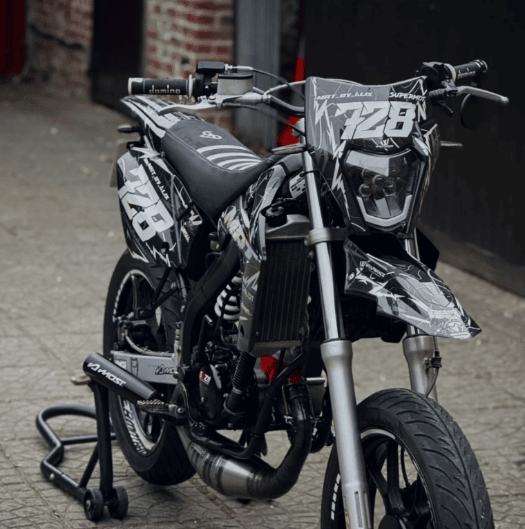 Moto noire et blanche numéro 728 avec housse de selle BKS, garée en ville