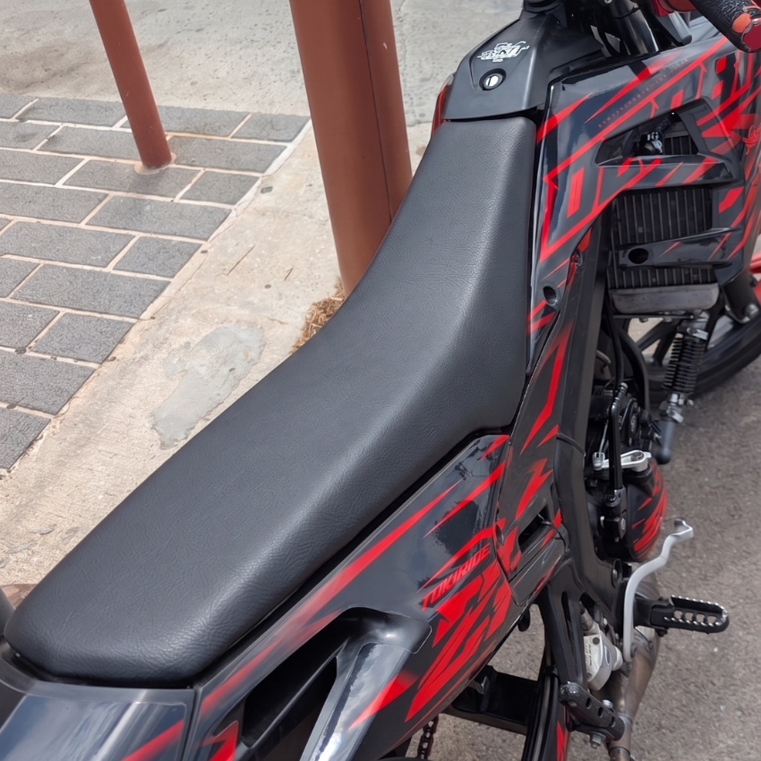 Une Rieju MRT 50 garée le long d’un trottoir, avec sa selle d’origine noire et lisse